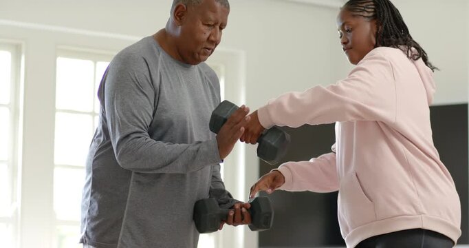 African American senior father with daughter handing hex dumbbell, coaching curls in home workout