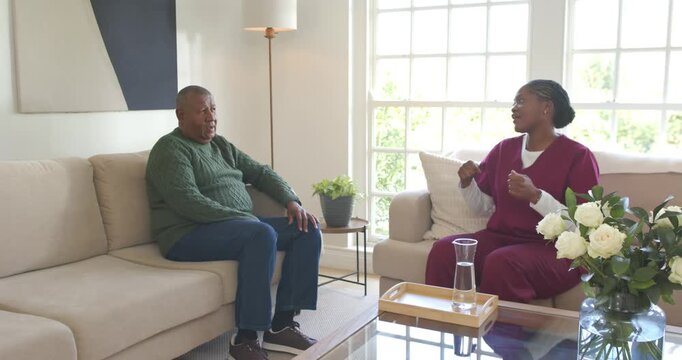 African American woman in scrubs replying while man near carafe sharing health concerns at home