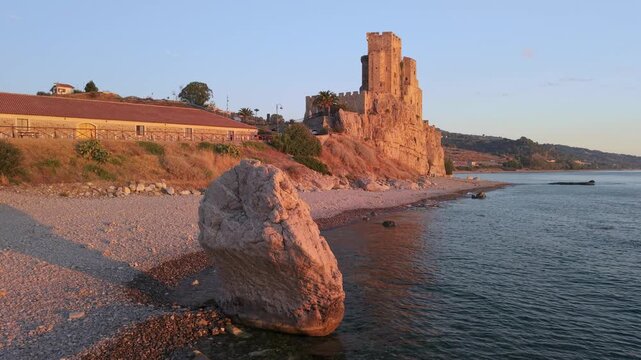 Castello Federiciano anvil rock sunrise aerial tilt up in Roseto Capo Spulico 4K. Scoglio dell Incudine and castle reflection on sea at pink morning light. Empty beach in Calabria Italy