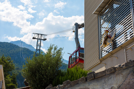 Scenic view of a cable car ascending a mountain with lush greenery and a building featuring horizontal blinds under a bright blue sky with scattered clouds