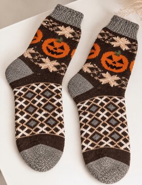 Cozy knitted Halloween socks with jack-o-lantern pumpkin patterns, warm autumn fashion accessories, festive seasonal clothing, geometric ornaments and soft wool texture on a white background