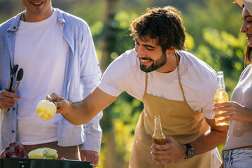Naklejka premium Man holding fresh ingredients while friends prepare food outdoors