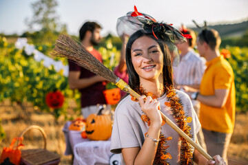 Naklejka premium Smiling woman holding a decorated broom at a Halloween vineyard party