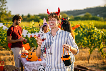 Naklejka premium Man wearing devil horns holding a wine glass during an outdoor Halloween party