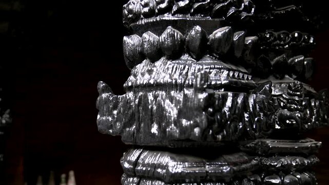 Detailed close-up shot of a traditional ornate black wooden pillar, highlighting the intricate carvings and glossy finish of the craftsmanship against a dark, atmospheric background in Nepal temple