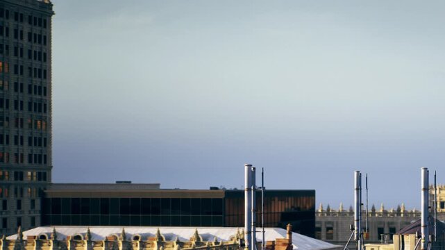Against a clear sky, modern structures rise alongside historic buildings. Rooftops and chimneys create an interesting silhouette in a vibrant city scene during the day.