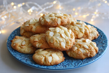 Italian pignoli cookies (pine nut cookies) on a blue plate before plain ivory background with white christmas lights © britaseifert