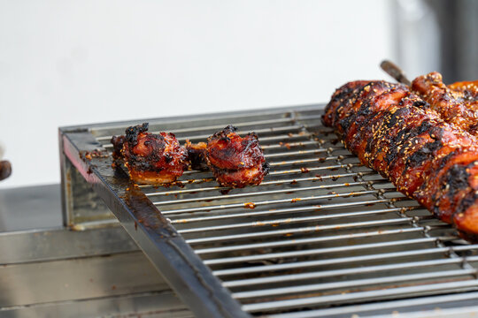 Juicy, dark glazed meat pieces cooking on a stainless steel grill rack at a street food market. The sweet and spicy marinade with sesame adds a crispy texture.