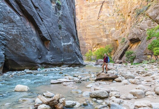 Hiker standing on a rock next to a river, Zion Narrows, narrow of the Virgin River, steep faces of Zion Canyon, Zion National Park, Utah, USA