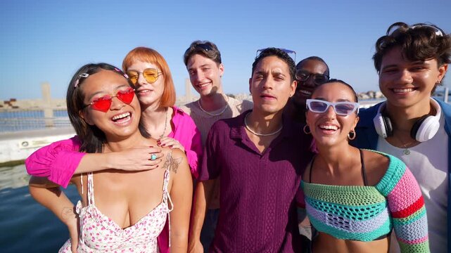 Group of stylish and diverse friends smiling and making funny faces while taking a selfie video together outdoors, capturing a joyful and memorable moment on a beautiful sunny summer vacation