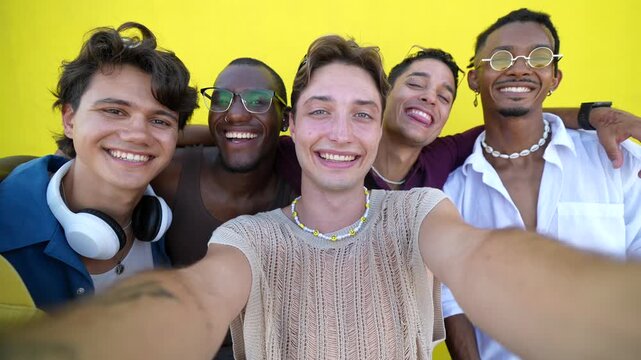 Group of young multiethnic male friends standing together in front of a yellow wall, smiling and having fun while taking a selfie, showing friendship, togetherness, and happiness