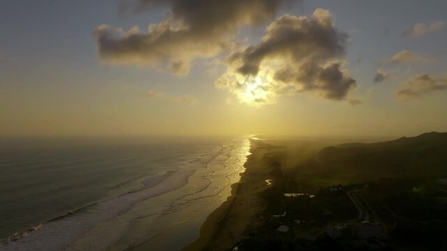 Aerial view of Parangtritis Beach at sunset with golden light reflecting on the waves and the coastline, Kecamatan Kretek, Daerah Istimewa Yogya, Indonesia.