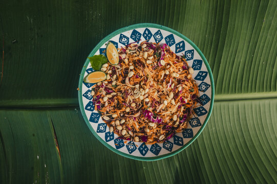 View of a vibrant salad with shredded carrots, red cabbage, and peanuts served on a patterned bowl atop a green banana leaf in Puerto Viejo de Talamanca, Limon Province, Costa Rica.
