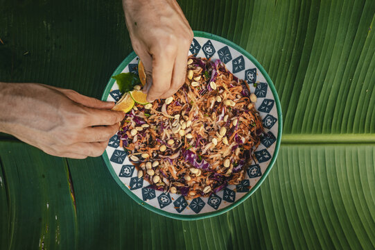 View of hands squeezing lime over a bowl of salad with red cabbage, carrots, and peanuts on a banana leaf in Puerto Viejo de Talamanca, Limon Province, Costa Rica.