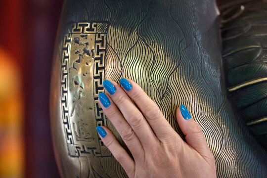 Woman touches polished brass crane sculpture for good luck inside Temple of Literature. Hanoi. Vietnam.