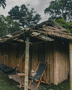 View of a rustic bamboo hut with a thatched roof, featuring a hammock and a chair on a deck surrounded by lush tropical greenery in Puerto Viejo de Talamanca, Limon Province, Costa Rica.