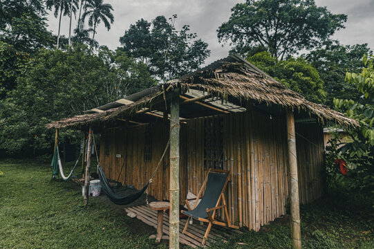 View of a rustic bamboo cabin with a thatched roof, hammocks, and a wooden chair on a deck, surrounded by lush tropical vegetation in Puerto Viejo de Talamanca, Limon Province, Costa Rica.