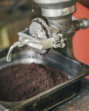 View of a manual coffee grinder processing roasted beans into fresh grounds falling into a metal tray, Puerto Viejo de Talamanca, Limon Province, Costa Rica.