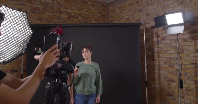 Female presenter on set holding mic as operator framing camera and crew checking sound