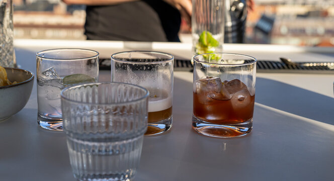 Bartender muddles fresh lime in a tall glass to prepare a cocktail at a sunny rooftop bar with a city view