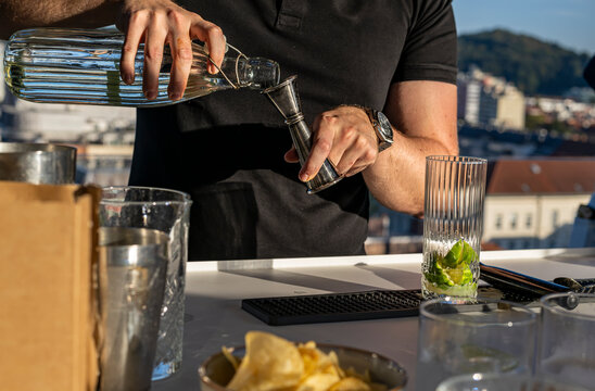 Fresh lime and citrus are muddled in a tall glass for a cocktail on a rooftop bar overlooking the city
