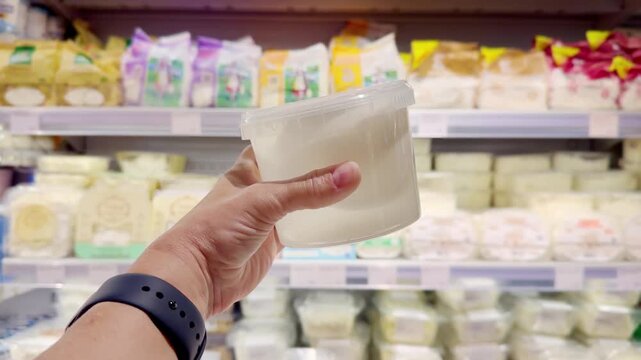 Hand Holding Cottage Cheese in Supermarket &ndash; Dairy Products in Front of Blurred Shelves