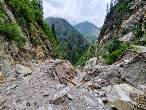 View of the rugged mountain path in Malana showing signs of a recent landslide with rocky debris, steep cliffs, and lush pine forests in Malana, Himachal Pradesh, India.