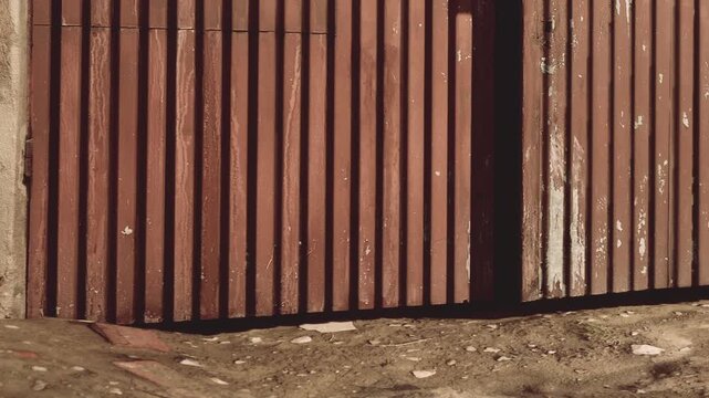 A charming wooden gate stands ajar, inviting in the soft light of the afternoon. The earthy path suggests a quiet neighborhood with hints of nature and history surrounding it.