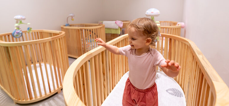 Happy toddler standing and playing in a stylish crib within a modern nursery filled with wooden cribs