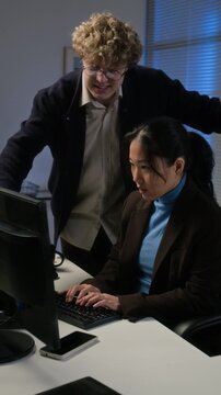 Vertical video of Asian young adult woman typing on computer while Caucasian young adult man assisting with coding. Clip suits software development ads and IT security campaigns