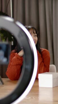 Vertical video: Camera rolling woman in orange knit facing co-host, filming by ringlight
