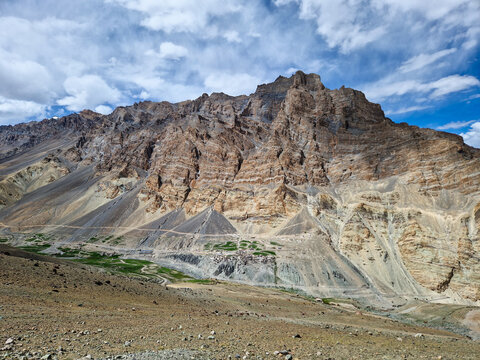 View of Penzi La road winding through the rugged, rocky mountain landscape of Zanskar with layered cliffs and sparse green vegetation in Zanskar, Ladakh, India.