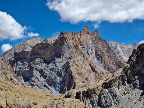 View of Penzi La road winding through the rugged, rocky mountains of the Zanskar range under a bright blue sky with scattered clouds in Zanskar, Ladakh, India.