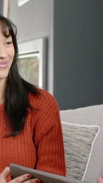 Vertical video: Panning woman rust sweater holding tablet at home, man with specs chatting on couch