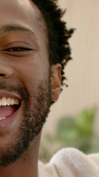 Vertical video: Smiling man in cream sweater reacting to phone at home, covering lens, copy space