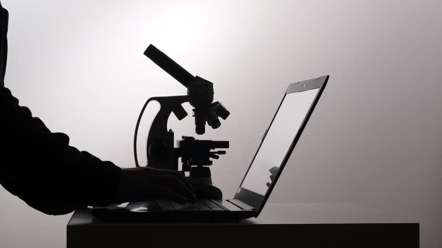 Scientist hands typing on a laptop next to a microscope, representing digital innovation, research, education, and analysis in a scientific laboratory setting