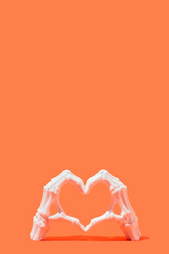 Skeletal hand in the heart shape on a orange background with copy space. Vertical design.