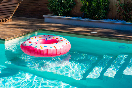 Pink donut inflatable float in turquoise swimming pool with submerged steps and wooden deck