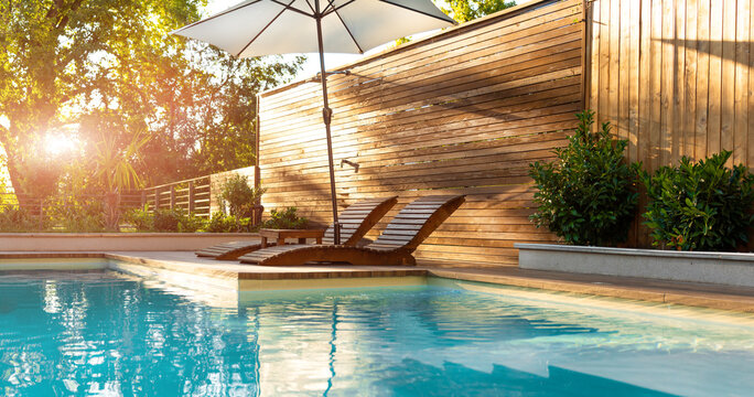 Modern Villa Pool with Wooden Sunbeds and Palm Trees at Sunset. Concept of upscale leisure and comfort in a stylish outdoor area