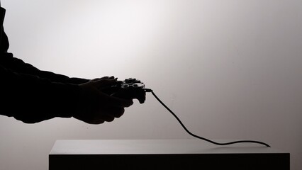 Silhouette of a person holding a wired gamepad, engaging in online gaming or e sports, representing technology, entertainment, and digital lifestyle with a focus on human interaction © Aliaksandr