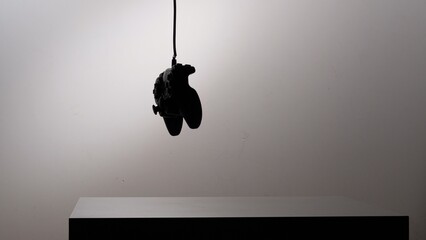 Silhouette of a game controller hanging from a cable in a minimalist studio setting, representing concepts of gaming addiction, dependency, and the struggles with virtual worlds © Aliaksandr
