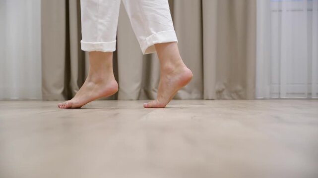 Young woman walking tiptoe barefoot on a warm wooden floor at home, Slow motion