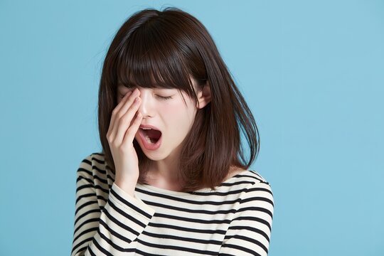 寝起きの眠い若い女性が目元を擦り大きくあくびをする瞬間