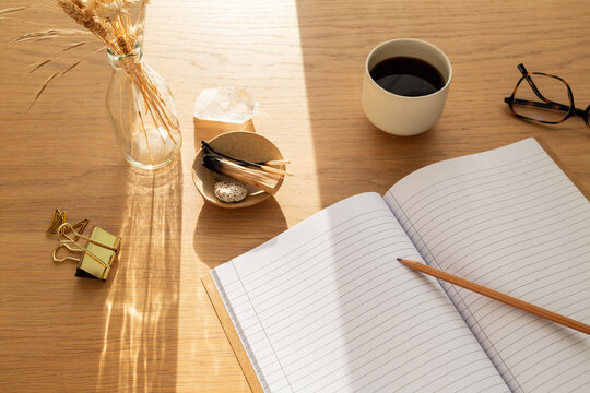 Bureau en bois ensoleill&eacute; avec cahier ouvert, tasse de caf&eacute;, fleurs s&eacute;ch&eacute;es et palo santo