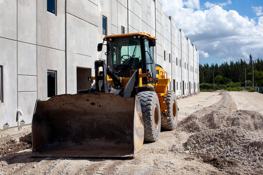 Heavy duty industrial wheel loader parked next to a precast concrete warehouse building under construction