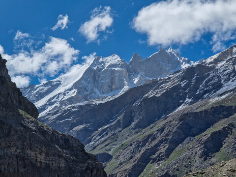 View of the rugged snow-capped peaks and rocky slopes near the Penzi La road in the Zanskar valley under a bright blue sky with scattered clouds, Zanskar, Ladakh, India.