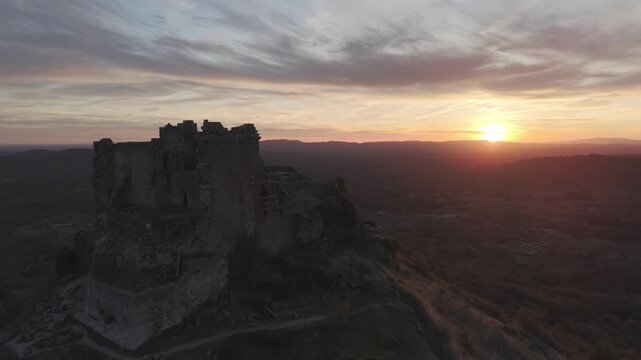 Aerial view of the historic stone ruins of Trevejo Castle silhouetted against a vibrant sunset sky, overlooking the rolling landscape of Trevejo, Extremadura, Spain.