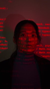 Vertical portrait of young adult Asian woman opening eyes and looking at camera with projected computer code. Footage suitable for cybersecurity marketing and artificial intelligence technology ads