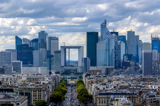 View of the modern skyscrapers of La Defense skyline with the Grande Arche in the center, set against a cloudy blue sky above the urban landscape of Paris, Ile-de-France, France.
