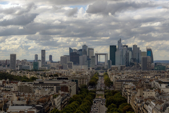 View of the La Defense skyline featuring modern glass skyscrapers and the Grande Arche rising above the historic urban landscape and tree-lined avenues in Paris, Ile-de-France, France.